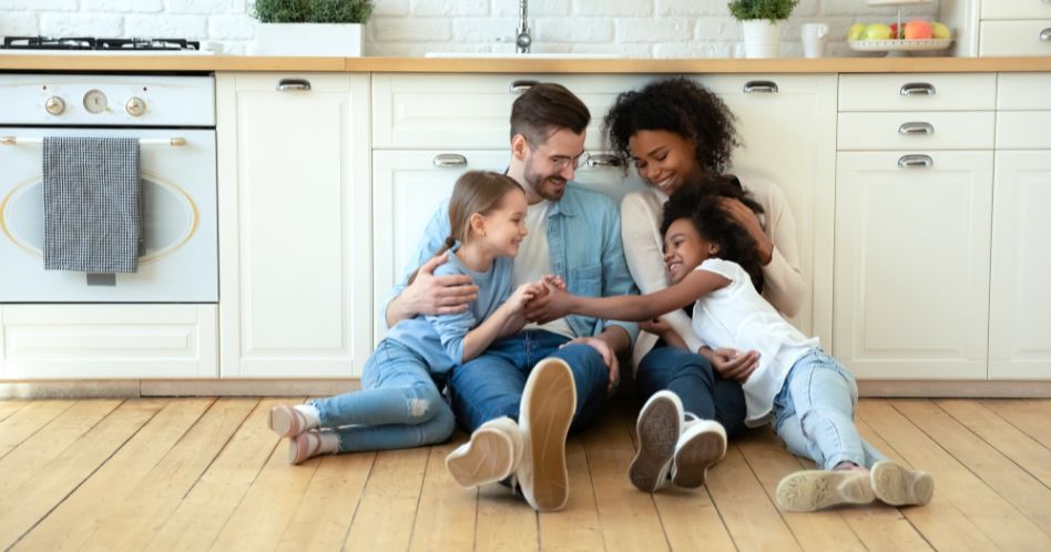 smiling multiracial family sitting on kitchen floor 948x498